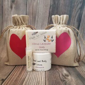 A bar of soap, jar of lotion and lip balm in front of 2 linen gift bags with hearts on them